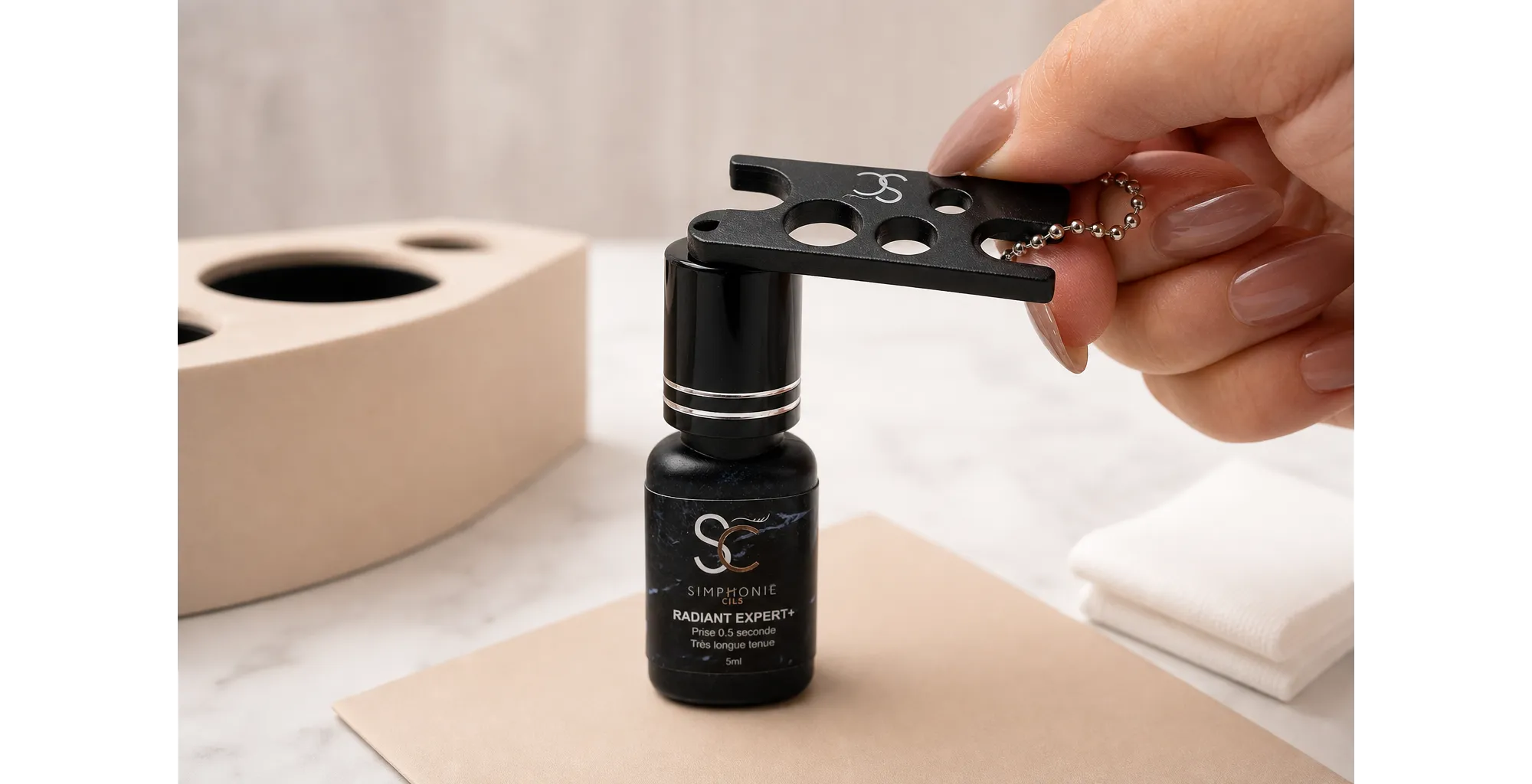 Gros plan d’une professionnelle utilisant le Décapsuleur à colle sur le bouchon propre d’un flacon de Colle Radiant Expert+ posé sur une protection de travail.